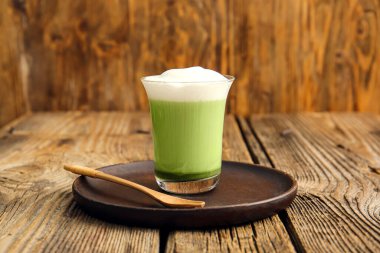 Bir bardak dalgona matcha latte ve tahta arka planda kaşık