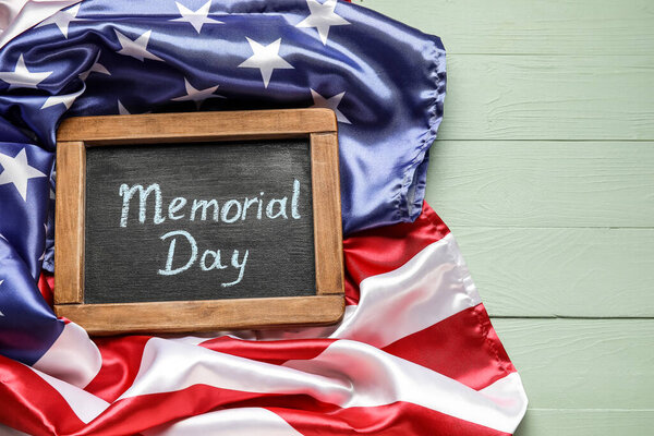 Chalkboard with text MEMORIAL DAY and USA flag on color wooden background