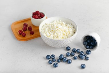 Açık arkaplanda bir kase süzme peynir, yabanmersini ve çilek