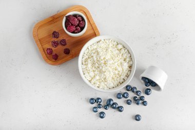 Açık arkaplanda bir kase süzme peynir, yabanmersini ve çilek