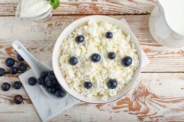 Hafif ahşap arka planda yabanmersinli süzme peynir kasesi.