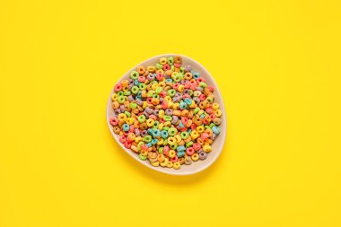 Renkli arkaplanda lezzetli mısır gevreği halkaları olan bir kase