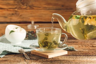 Çaydanlıktan, tahtadan arka planda fincana yeşil çay dökülüyor.