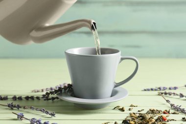 Çaydanlıktan fincana renkli ahşap arka planda yeşil çay dökülüyor.