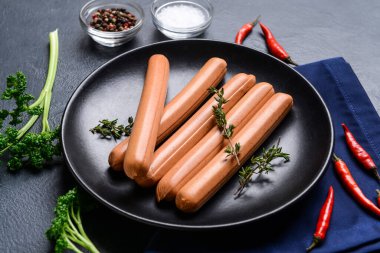 Koyu arkaplanda lezzetli sosisler, baharatlar ve otlarla dolu tabaklar.