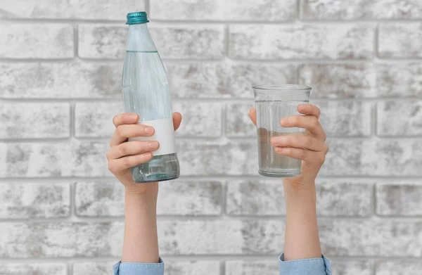 Weibliche Hände Mit Flasche Und Glas Wasser Auf Backsteinhintergrund — Stockfoto