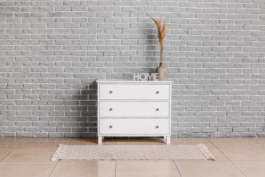 Odada tuğla duvarın yanında vazo ve dekor olan modern çekmeceler.