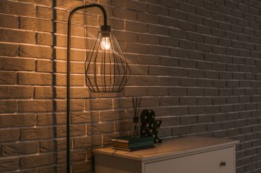 Parlayan modern lamba ve dekorlu çekmeceler tuğla duvarın yanında.