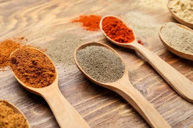 Ahşap arka planda farklı baharatlı kaşıklar, yakın plan.