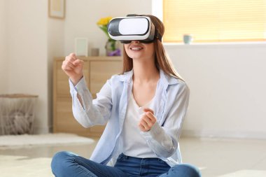 Evde sanal gerçeklik gözlüklü genç bir kadın var.