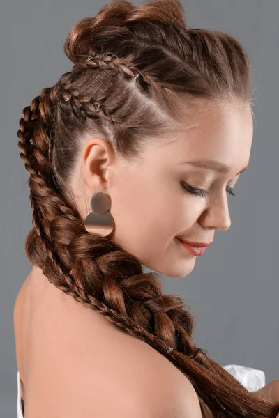 Beautiful young woman with braided hair on grey background