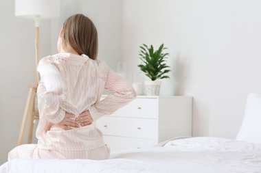 Yatak odasında sırt ağrısı çeken genç bir kadın.