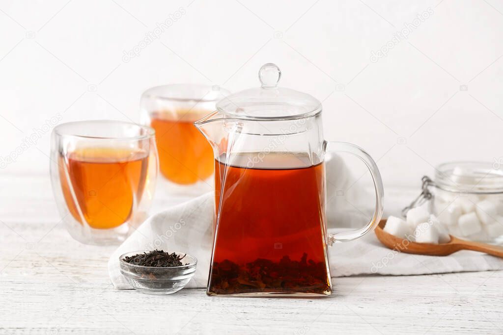 Teapot with hot tea and glasses on light background