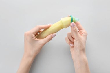 Gri arka planda kesik salatalıklı ve prezervatifli bir kadın eli. Erotik kavram