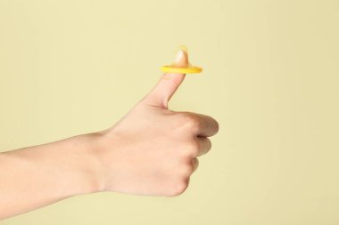 Renkli arka planda baş parmak hareketi gösteren prezervatifli bir kadın eli. Erotik kavram