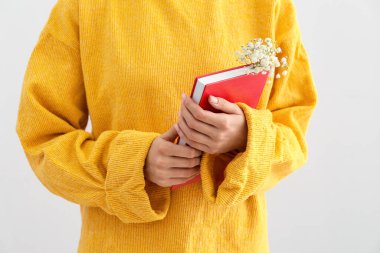 Işıklı arka planda taze çiçekli kitap tutan kadın, yakın plan.