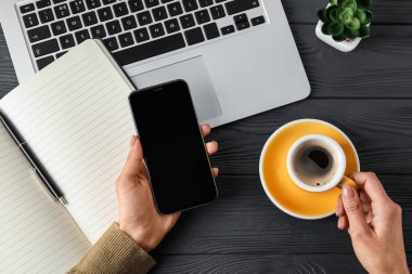 İş yerinde cep telefonu ve bir fincan kahve olan bir kadın.