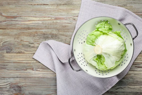 Colander with iceberg lettuce on wooden background