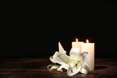 Candles with lily flowers on table against dark background clipart