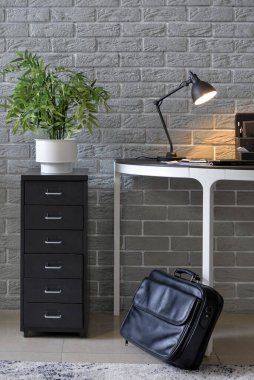 Odasında tuğla duvarın yanında valizi olan modern bir işyeri.