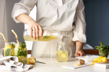 Kadın mutfaktaki mason kavanozuna limonata dolduruyor.