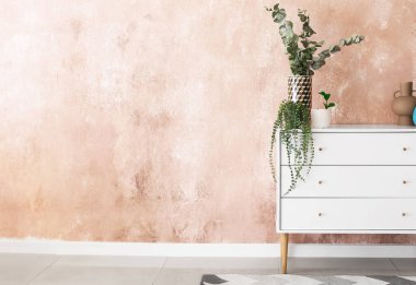 Renk duvarının yanında dekoru ve çiçekleri olan şık çekmeceler.