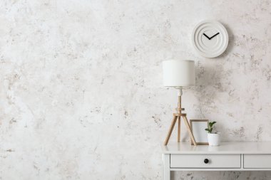Işık duvarı yakınında modern lamba, çerçeve ve bitki içeren masa