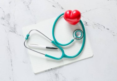 Işık arka planında kalp ve defter olan modern steteskop