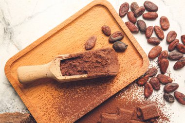 Açık arkaplanda kakao tozu ve fasulye kepçesi.