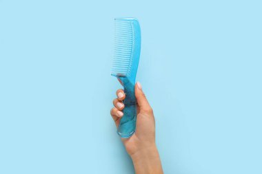 Arkaplanda plastik saç tarağı olan bir kadın el.