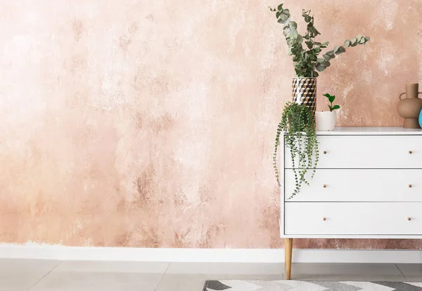 Renk duvarının yanında dekoru ve çiçekleri olan şık çekmeceler.