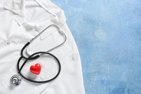 Stethoscope, heart and doctor's uniform on color background