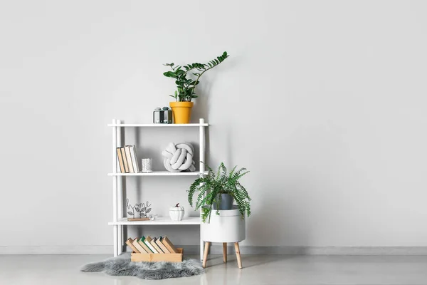 Modern shelf unit with books and houseplants near white wall in room