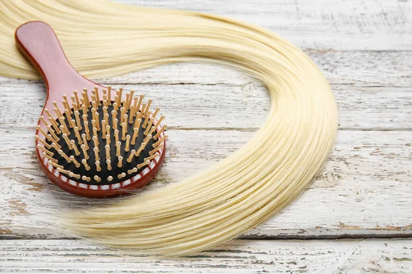 Hair brush with strand on white wooden background