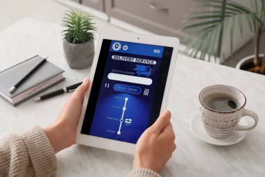 Evde elinde tablet bilgisayarı olan bir kadın teslimat hizmeti başvurusunun açık sayfasını tutuyor