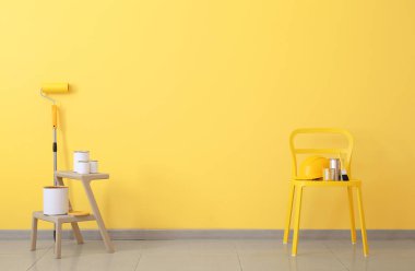 Renkli duvarın yanında boyacı aletleri olan merdiven ve sandalye.