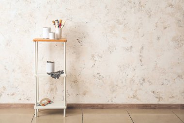 Işık duvarının yanında boya, fırça ve eldiven dolu raflar.