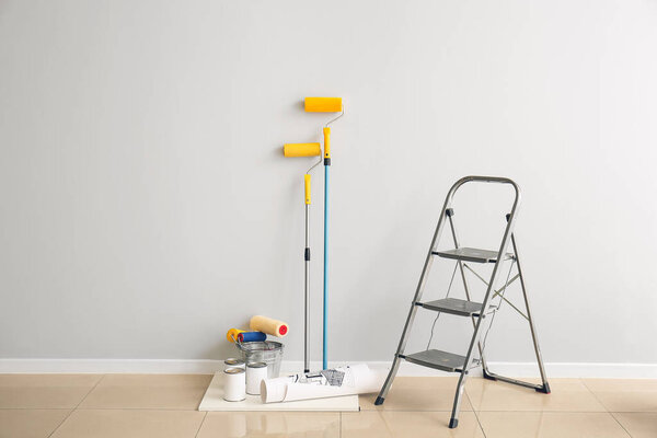 Ladder, cans of paints and rollers near light wall