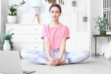Kilitleme sırasında laptoplu genç bir kadın evde yoga yapıyor.