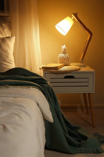 夜の部屋に光るランプ付きの大きな快適なベッドとテーブル — ストック写真