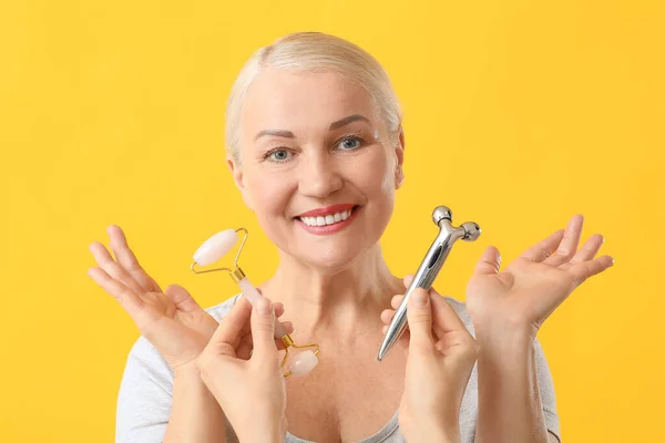 Reife Frau Mit Gesichtsmassagewerkzeugen Auf Farbigem Hintergrund — Stockfoto