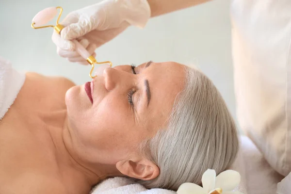 Mature woman receiving face massage in beauty salon