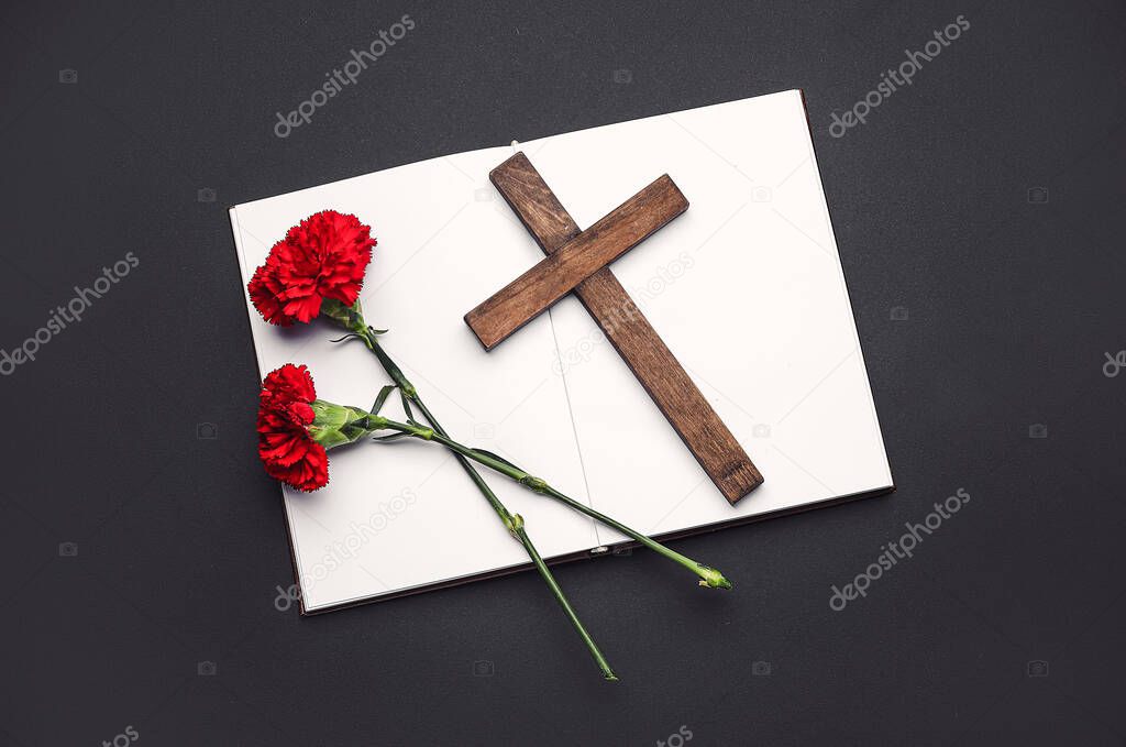 Carnation flowers with cross and book on dark background