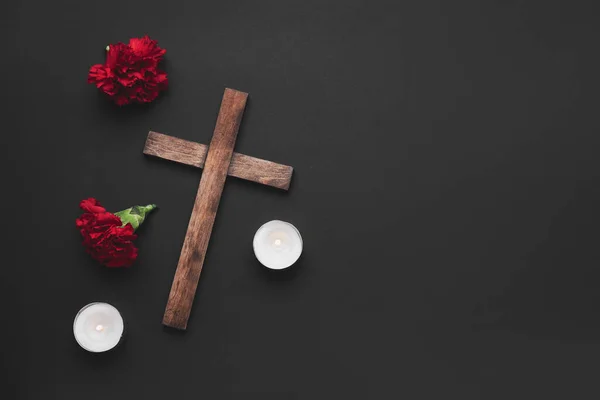 暗い背景にカーネーションの花やろうそくと木製の十字架 — ストック写真