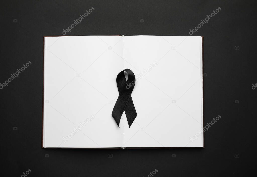 Black funeral ribbon with book on dark background