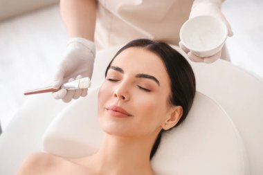 Güzellik salonunda kadının yüzüne maske takan bir kozmetikçi.