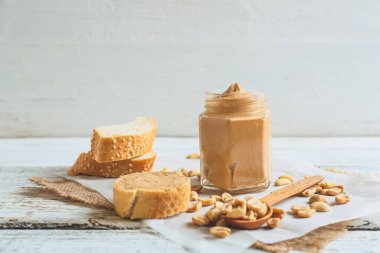 Hafif ahşap arka planda fıstık ezmeli kavanoz ve ekmek.