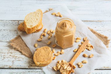 Hafif ahşap arka planda fıstık ezmeli kavanoz ve ekmek.