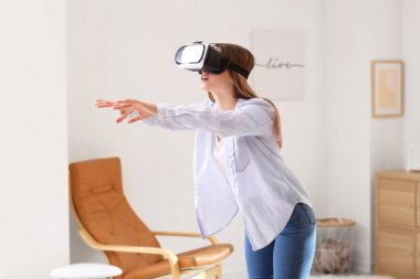 Evde sanal gerçeklik gözlüklü genç bir kadın var.