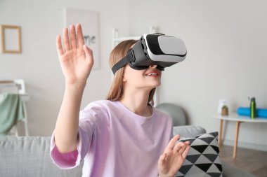 Evde sanal gerçeklik gözlüklü genç bir kadın var.